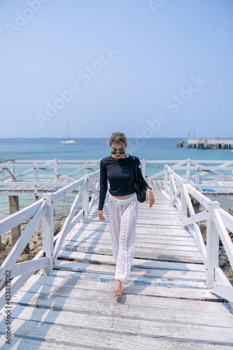 Traveler woman in swimsuit relaxing on white bridge looking sea beach.