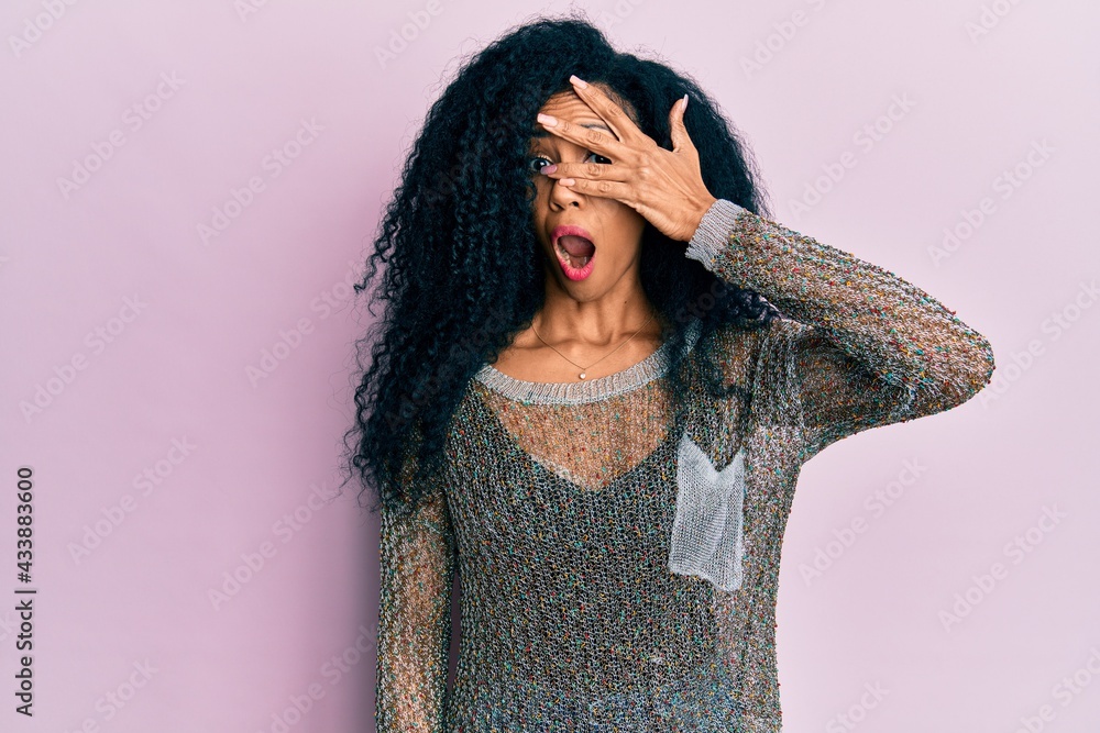 Middle age african american woman wearing casual clothes peeking in shock covering face and eyes with hand, looking through fingers afraid Middle age african american woman wearing casual clothes peeking in shock covering face and eyes with hand, looking through fingers afraid