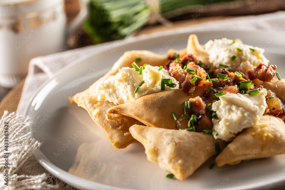 Fried pierogi served on a plate with bryndza cheese, bacon, and chives Fried pierogi served on a plate with bryndza cheese, bacon, and chives