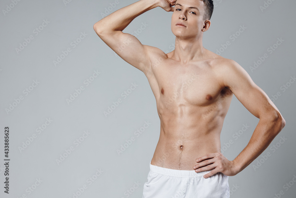 Fototapeta premium athlete in white shorts holds his hand above his head on a gray background and pumped up muscles
