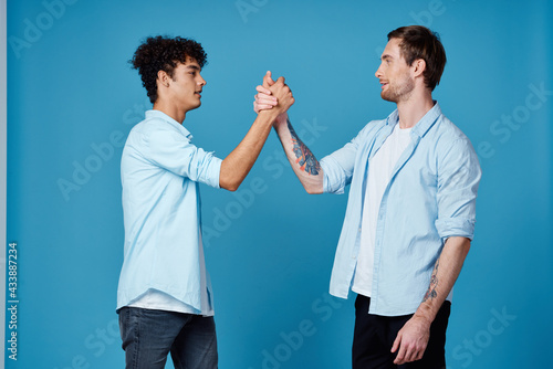 Happy friends in identical shirts shake hands on a blue background communication