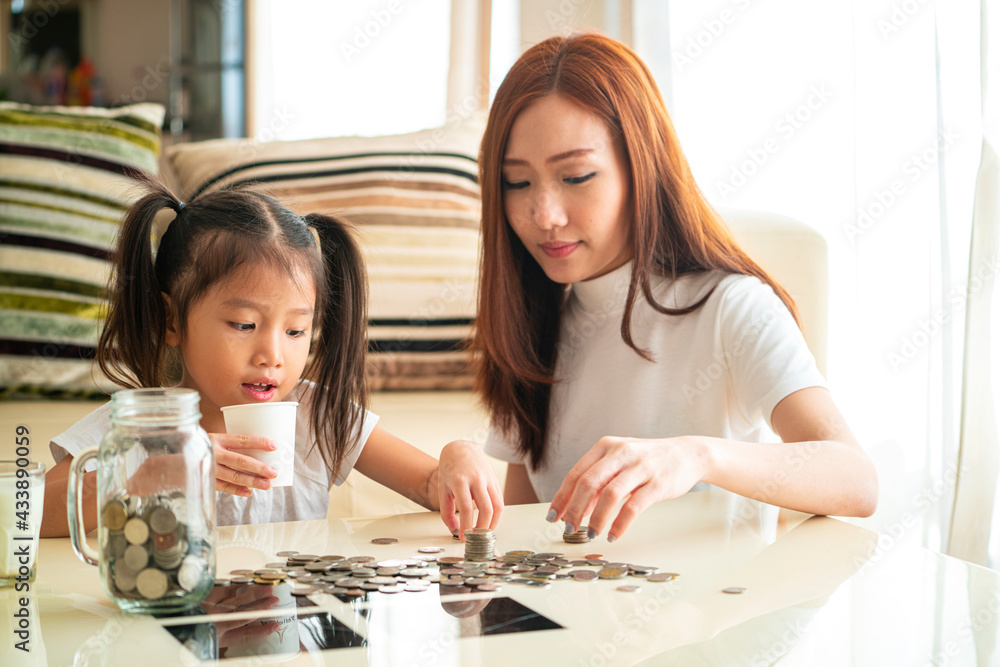 Banner photo of Asian family teach their daughter to saving money and putting coins into glass bank spend a quality time together. Asian family, relationship, happiness and investment concept Banner photo of Asian family teach their daughter to saving money and putting coins into glass bank spend a quality time together. Asian family, relationship, happiness and investment concept