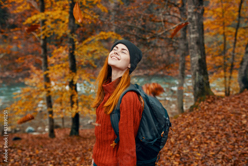 woman in a hat with a backpack and a sweater is resting in the autumn forest near the river in nature