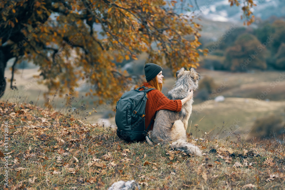 woman hiker with a backpack next to a dog admires the nature of the mountain