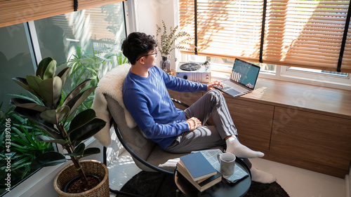 Young asian male tech user relaxing  holding laptop computer and looking at the screen in living room, Remote Job or work from home concept. photo