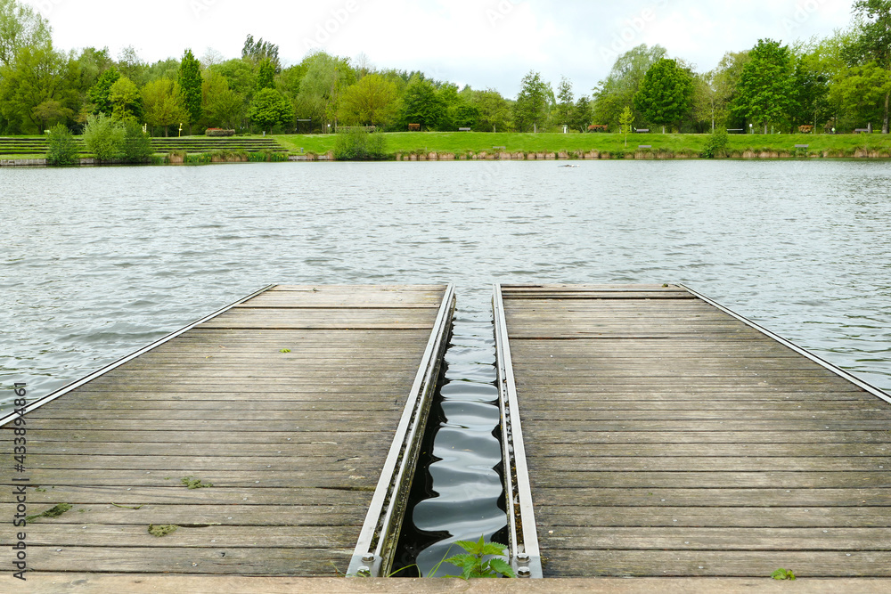 View of a double wooden pontoon by a lake in summer. Lush vegetation in the background.