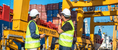 worker working with radio transceiver for controlling crane to loading container box to container ship in port shipping containers. logistics, sea transportation and logistics business concept photo