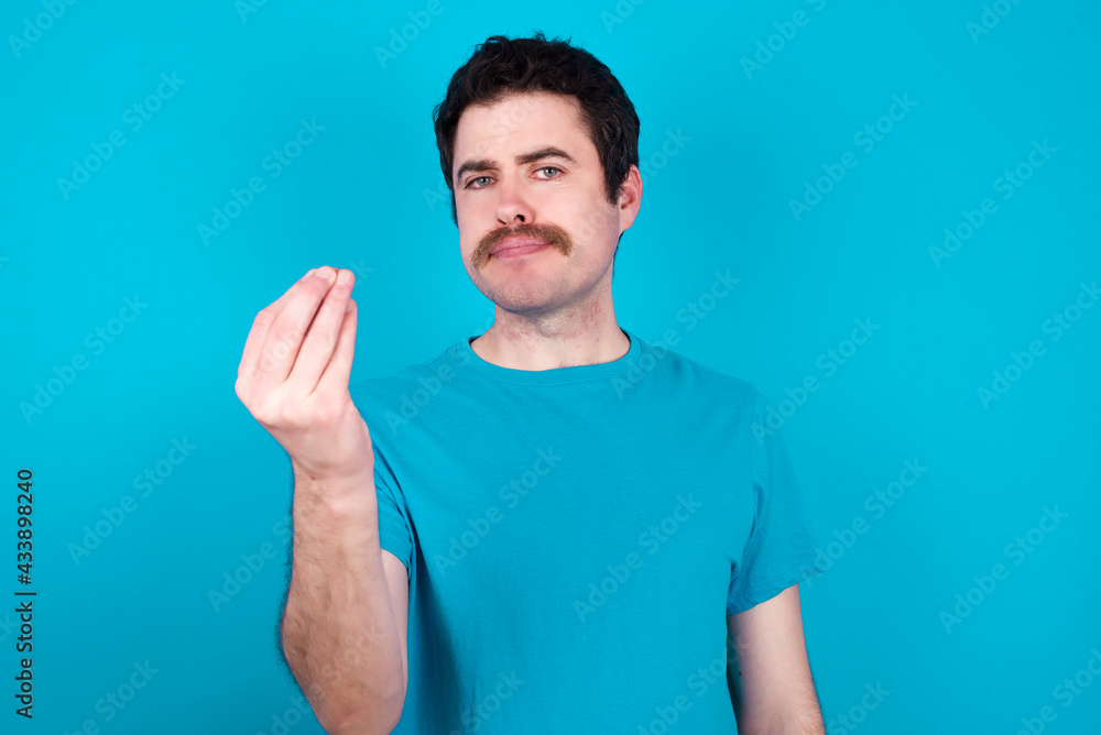young handsome Caucasian man with moustache wearing blue t-shirt against blue background Doing Italian gesture with hand and fingers confident expression young handsome Caucasian man with moustache wearing blue t-shirt against blue background Doing Italian gesture with hand and fingers confident expression