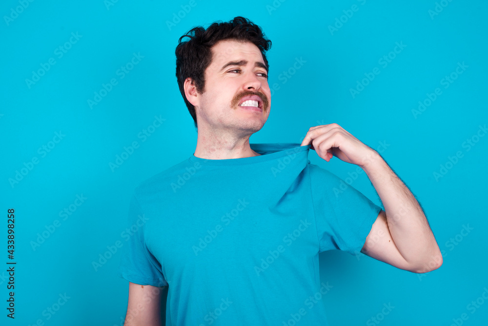 young handsome Caucasian man with moustache wearing blue t-shirt against blue background stressed, anxious, tired and frustrated, pulling shirt neck, looking frustrated with problem young handsome Caucasian man with moustache wearing blue t-shirt against blue background stressed, anxious, tired and frustrated, pulling shirt neck, looking frustrated with problem
