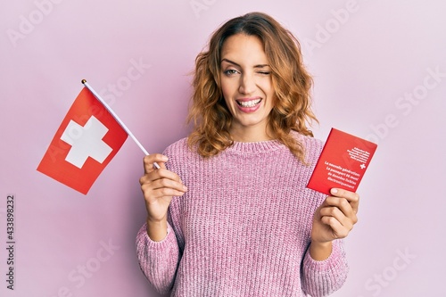 Young caucasian woman holding swiss flag and passport winking looking at the camera with sexy expression, cheerful and happy face. © Krakenimages.com
