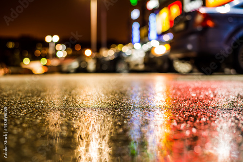 Rainy night in the parking shopping mall, rows of parked cars in the light of advertising. Close up view from the asphalt level