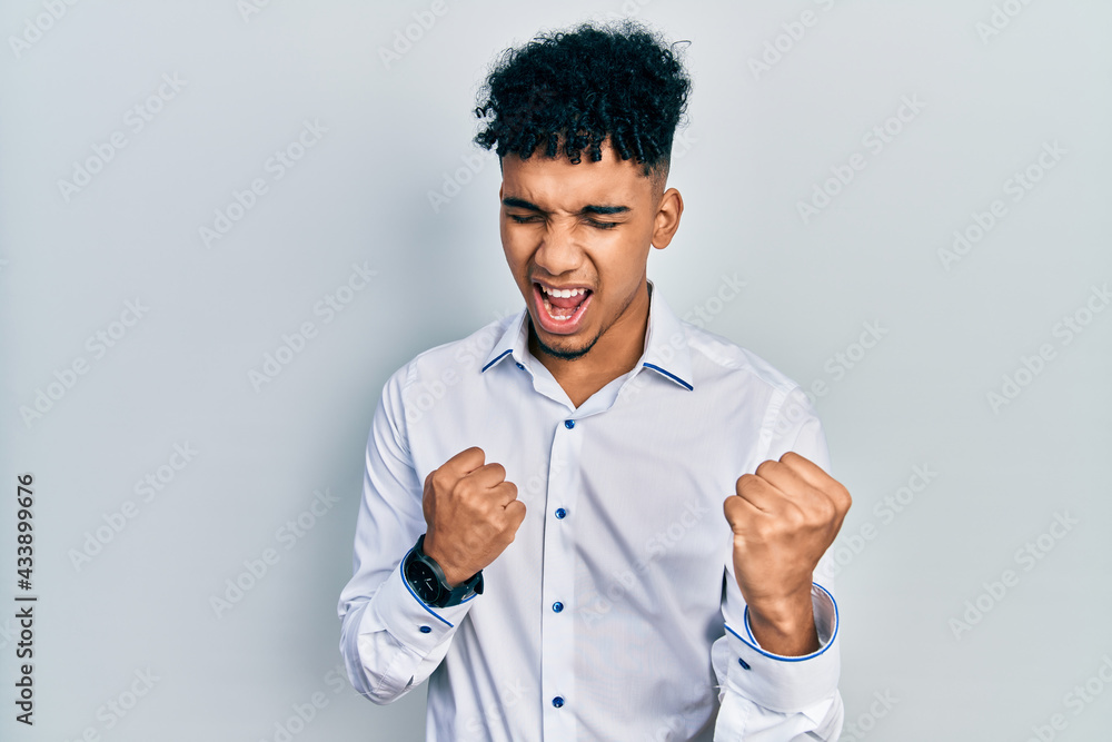 Young african american man wearing business shirt celebrating surprised and amazed for success with arms raised and eyes closed Young african american man wearing business shirt celebrating surprised and amazed for success with arms raised and eyes closed