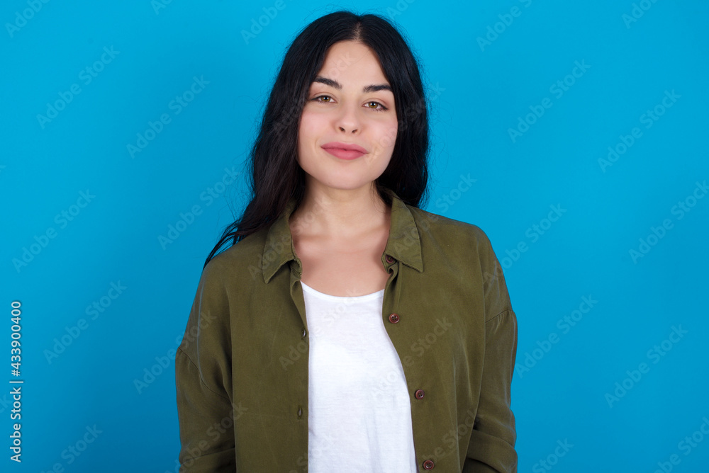 Happy young beautiful tattooed girl standing against blue wall looking at camera with charming cute smile. Happy young beautiful tattooed girl standing against blue wall looking at camera with charming cute smile.