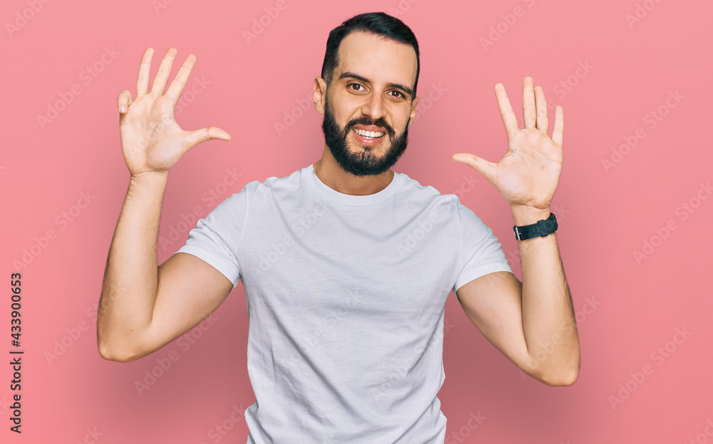 Young man with beard wearing casual white t shirt showing and pointing up with fingers number nine while smiling confident and happy. Young man with beard wearing casual white t shirt showing and pointing up with fingers number nine while smiling confident and happy.