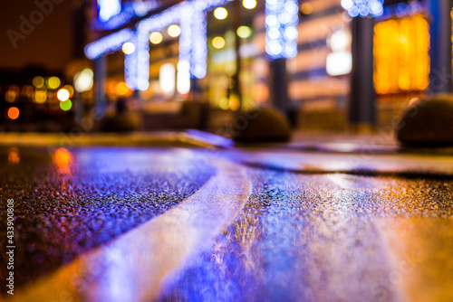 Rainy night in the parking shopping mall, illumination lights are reflected in a asphalt. Close up view from the level of the dividing line