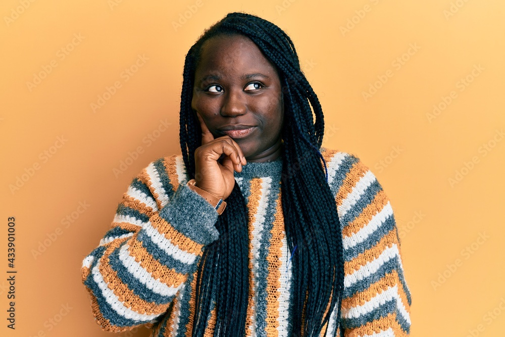 Young black woman with braids wearing casual winter sweater with hand on chin thinking about question, pensive expression. smiling and thoughtful face. doubt concept. Young black woman with braids wearing casual winter sweater with hand on chin thinking about question, pensive expression. smiling and thoughtful face. doubt concept.