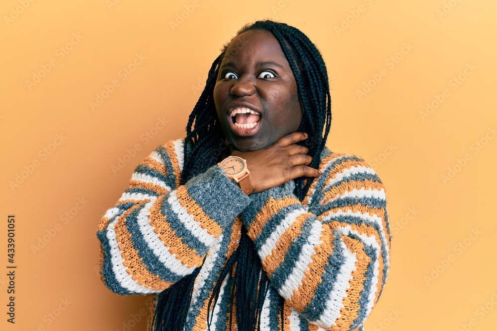 Young black woman with braids wearing casual winter sweater shouting suffocate because painful strangle. health problem. asphyxiate and suicide concept. Young black woman with braids wearing casual winter sweater shouting suffocate because painful strangle. health problem. asphyxiate and suicide concept.