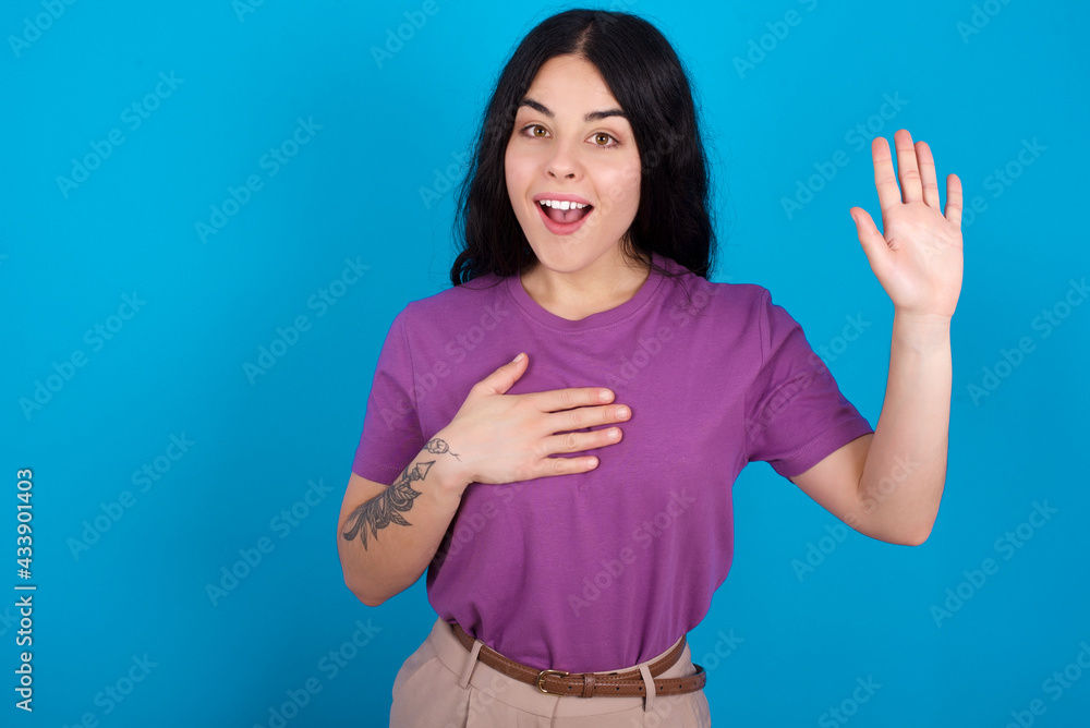 I swear, promise you not regret. Portrait of sincere young beautiful tattooed girl wearing purple t-shirt raising one arm and hold hand on heart as give oath, telling truth, want you to believe. I swear, promise you not regret. Portrait of sincere young beautiful tattooed girl wearing purple t-shirt raising one arm and hold hand on heart as give oath, telling truth, want you to believe.