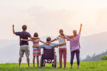 Rear view of group of family with Disabled handicapped man sitting in wheelchair having fun together outdoors