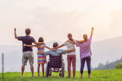 Rear view of group of family with Disabled handicapped man sitting in wheelchair having fun together outdoors