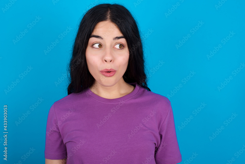 Shocked young beautiful tattooed girl wearing blue t-shirt standing against blue background look empty space with open mouth screaming: Oh My God! I can't believe this. Shocked young beautiful tattooed girl wearing blue t-shirt standing against blue background look empty space with open mouth screaming: Oh My God! I can't believe this.