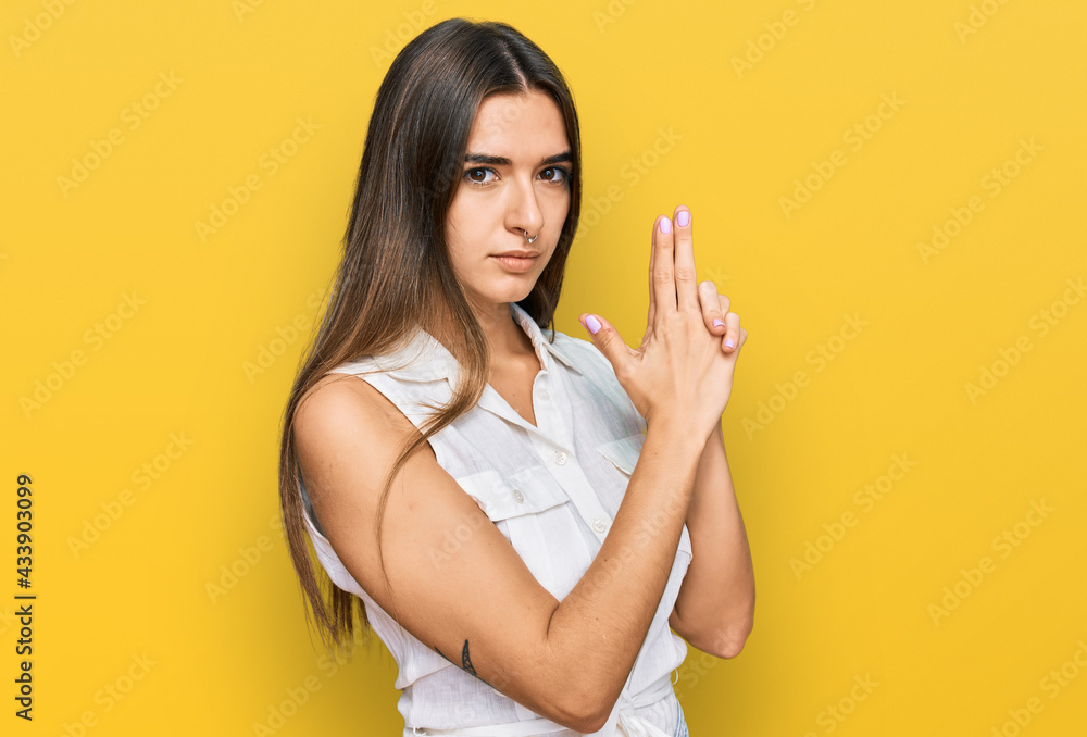 Young hispanic woman wearing casual clothes holding symbolic gun with hand gesture, playing killing shooting weapons, angry face Young hispanic woman wearing casual clothes holding symbolic gun with hand gesture, playing killing shooting weapons, angry face