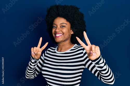 Young african american woman wearing casual clothes smiling looking to the camera showing fingers doing victory sign. number two.