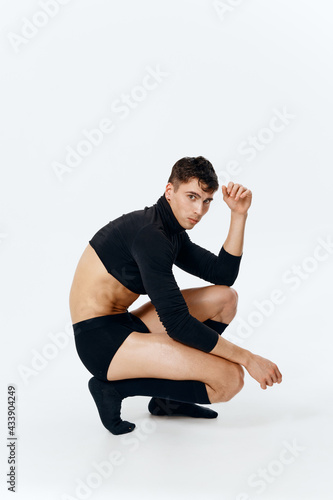 side view of a sporty man in shorts, socks and a sweater sits on a light background