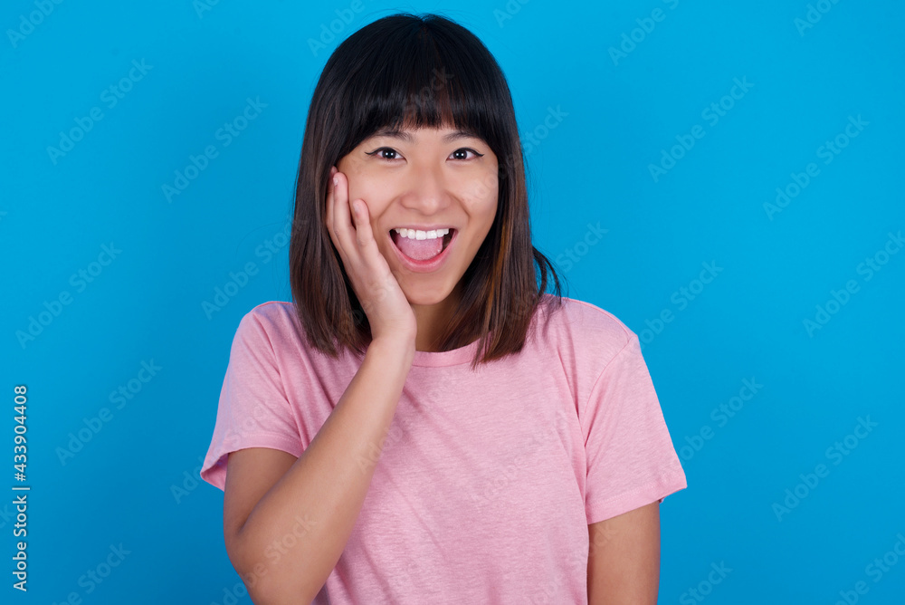 Shocked, astonished young beautiful asian woman wearing pink t-shirt looking surprised in full disbelief wide open mouth with hand near face. Positive emotion facial expression body language. Shocked, astonished young beautiful asian woman wearing pink t-shirt looking surprised in full disbelief wide open mouth with hand near face. Positive emotion facial expression body language.