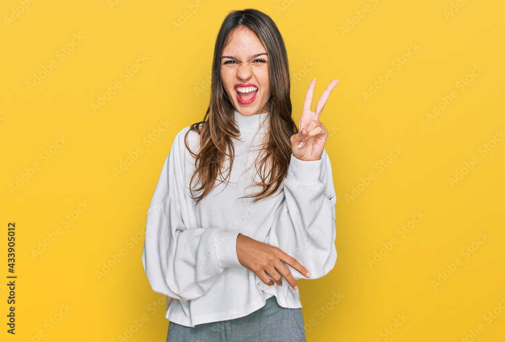 Young brunette woman wearing casual turtleneck sweater smiling with happy face winking at the camera doing victory sign. number two. Young brunette woman wearing casual turtleneck sweater smiling with happy face winking at the camera doing victory sign. number two.