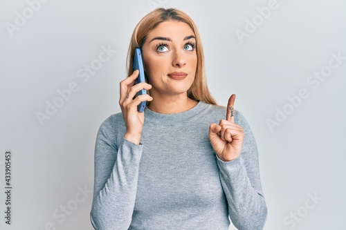 Young caucasian woman having conversation talking on the smartphone smiling with an idea or question pointing finger with happy face, number one