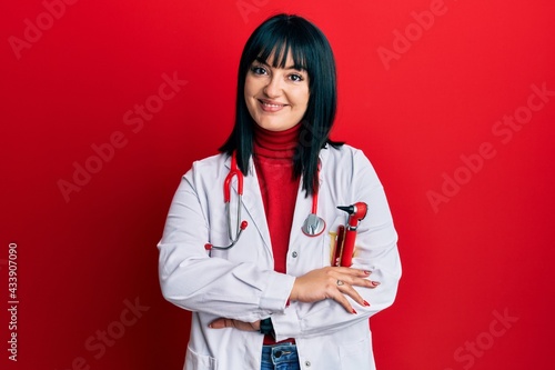 Young hispanic woman wearing doctor uniform and stethoscope happy face smiling with crossed arms looking at the camera. positive person.