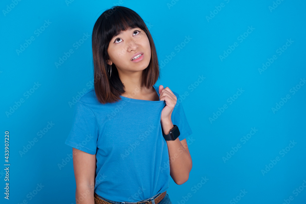 young beautiful asian girl wearing blue t-shirt against blue background stressed, anxious, tired and frustrated, pulling shirt neck, looking frustrated with problem young beautiful asian girl wearing blue t-shirt against blue background stressed, anxious, tired and frustrated, pulling shirt neck, looking frustrated with problem