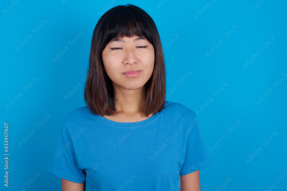 young beautiful asian girl wearing blue t-shirt against blue background nice-looking sweet charming cute attractive lovely winsome sweet peaceful closed eyes young beautiful asian girl wearing blue t-shirt against blue background nice-looking sweet charming cute attractive lovely winsome sweet peaceful closed eyes