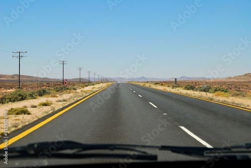 View of an empty road in South Africa, from inside of a car, on a sunny day, with blue sky and no clouds