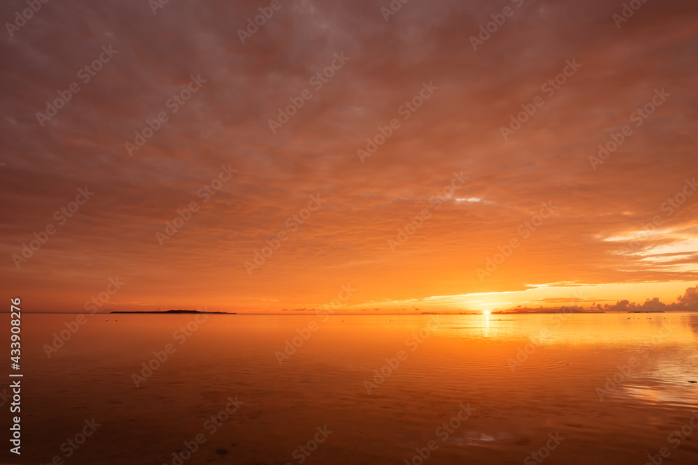 Radiant orange sunrise at a tropical island. Entire colorful sky reflected on smooth surface of the ocean. Iriomote Island, natural world heritage.