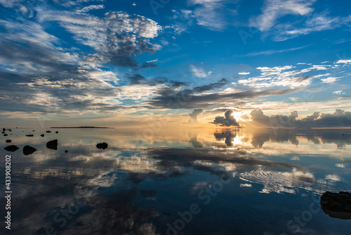 Breathtaking sunrise reflecting in the sea at Nakano beach, with beautiful white clouds and an orange horizon. Hatoma Island far away composing the scene, Iriomote Island. photo