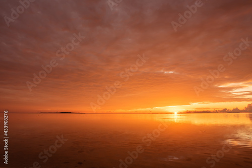 Radiant orange sunrise at a tropical island. Entire colorful sky reflected on smooth surface of the ocean. Iriomote Island  natural world heritage.