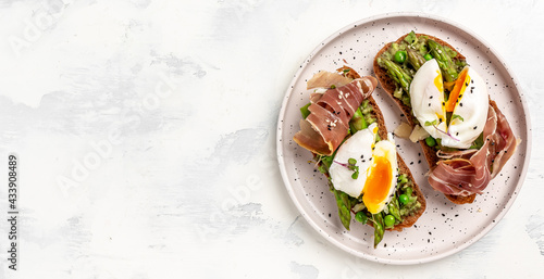 toasts with avocado, asparagus and Benedict Poached eggs with prosciutto on white plate, top view, Long banner format, top view