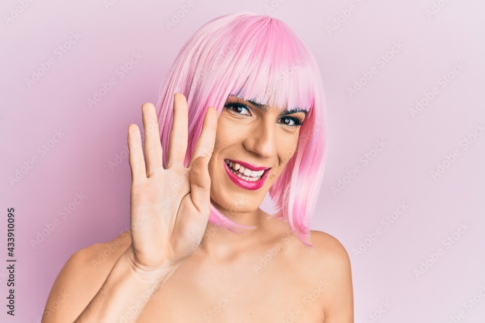 Young man wearing woman make up wearing pink wig showing and pointing up with fingers number four while smiling confident and happy. Young man wearing woman make up wearing pink wig showing and pointing up with fingers number four while smiling confident and happy.