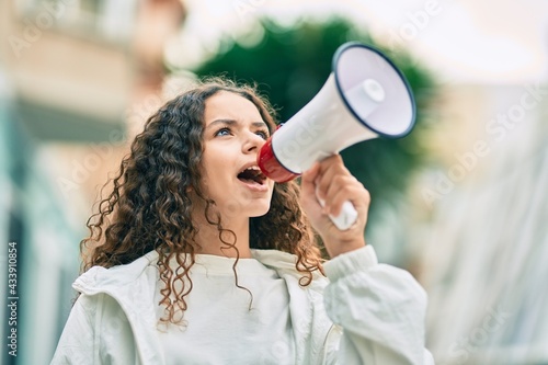 Hispanic child girl shouting angry using megaphone at the city. photo