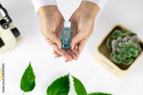 Принти на полотні Close-up hands hold cosmetic bottle with water-tonic on white lab background with microscope out of focus
