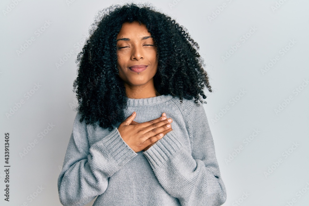 African american woman with afro hair wearing casual winter sweater smiling with hands on chest, eyes closed with grateful gesture on face. health concept. African american woman with afro hair wearing casual winter sweater smiling with hands on chest, eyes closed with grateful gesture on face. health concept.