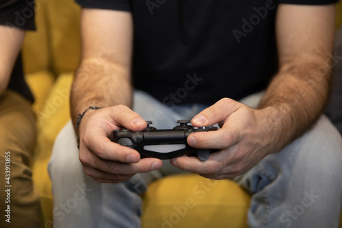 Hairy male gamer hands holding remote joystick close up. two guys intently Enjoying video game. man Playing Videogame sitting on comfy yellow sofa Resting At Home. Fans together  fun for two
