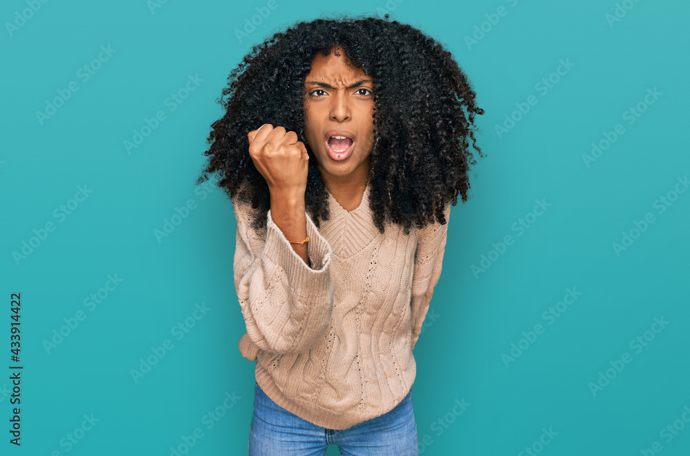 Young african american girl wearing casual clothes angry and mad raising fist frustrated and furious while shouting with anger. rage and aggressive concept. Young african american girl wearing casual clothes angry and mad raising fist frustrated and furious while shouting with anger. rage and aggressive concept.