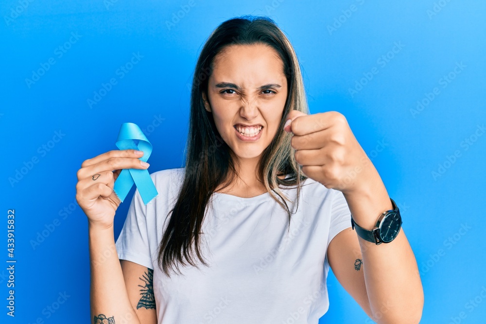 Young hispanic woman holding blue ribbon annoyed and frustrated shouting with anger, yelling crazy with anger and hand raised Young hispanic woman holding blue ribbon annoyed and frustrated shouting with anger, yelling crazy with anger and hand raised