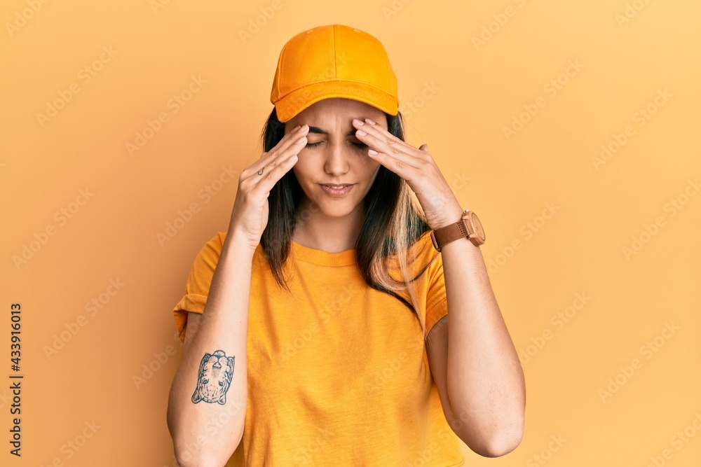 Young hispanic woman wearing delivery uniform and cap with hand on head for pain in head because stress. suffering migraine. Young hispanic woman wearing delivery uniform and cap with hand on head for pain in head because stress. suffering migraine.