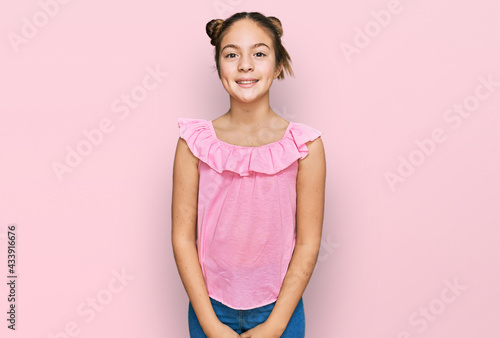 Beautiful brunette little girl wearing summer pink shirt looking positive and happy standing and smiling with a confident smile showing teeth