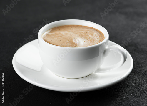 White cup with espresso coffee on a black background.