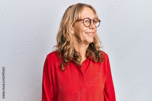 Middle age blonde woman wearing casual clothes and glasses looking to side, relax profile pose with natural face and confident smile.